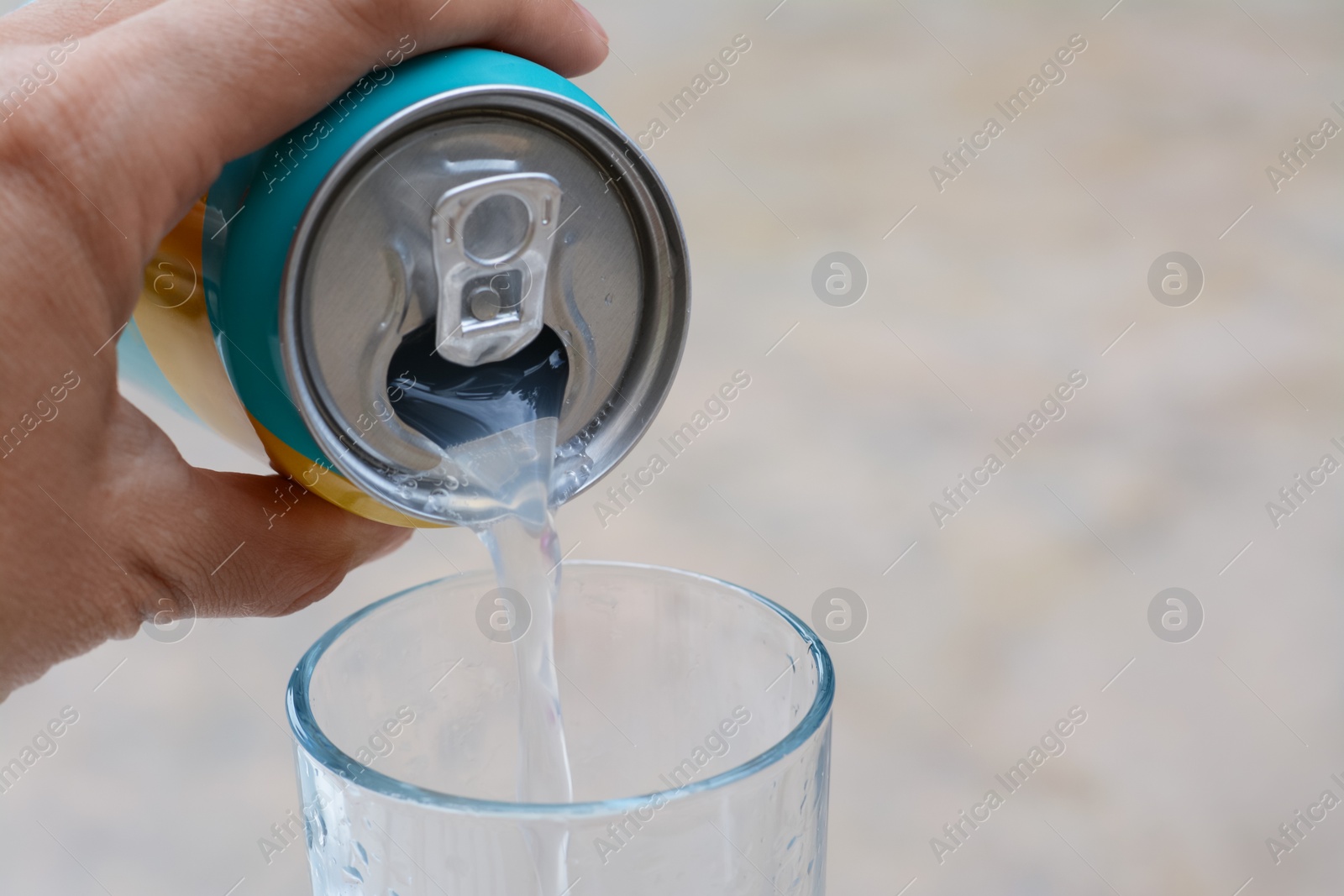 Photo of Woman pouring drink from aluminum can into glass on blurred background, closeup. Space for text