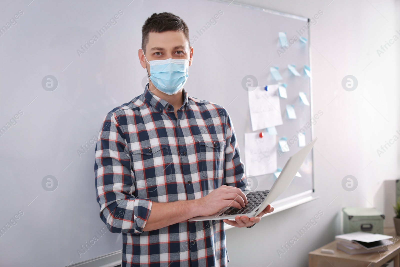 Photo of Teacher with protective mask and laptop near board in classroom. Reopening after Covid-19 quarantine