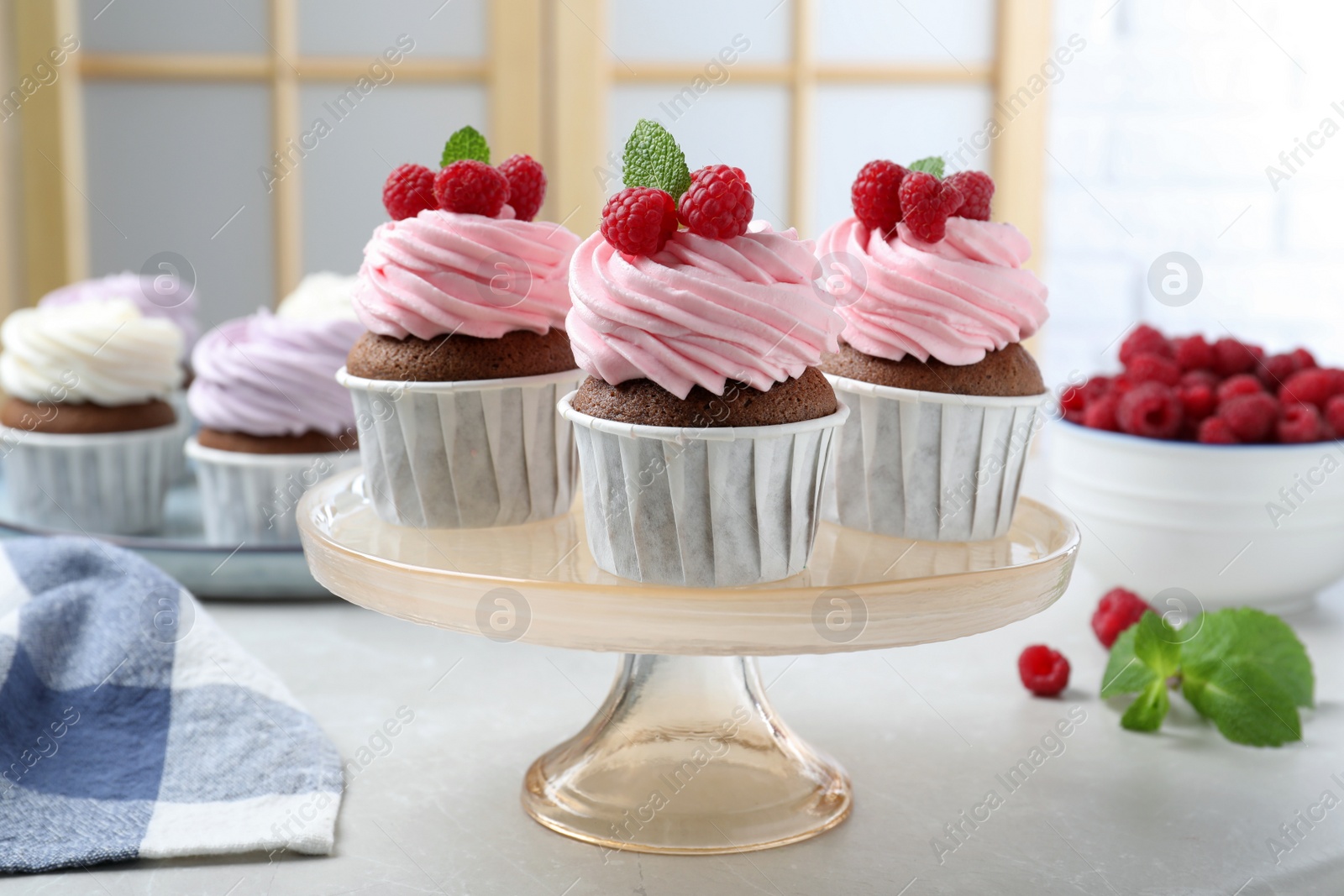 Photo of Delicious cupcakes with cream and raspberries on light table indoors