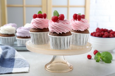 Delicious cupcakes with cream and raspberries on light table indoors