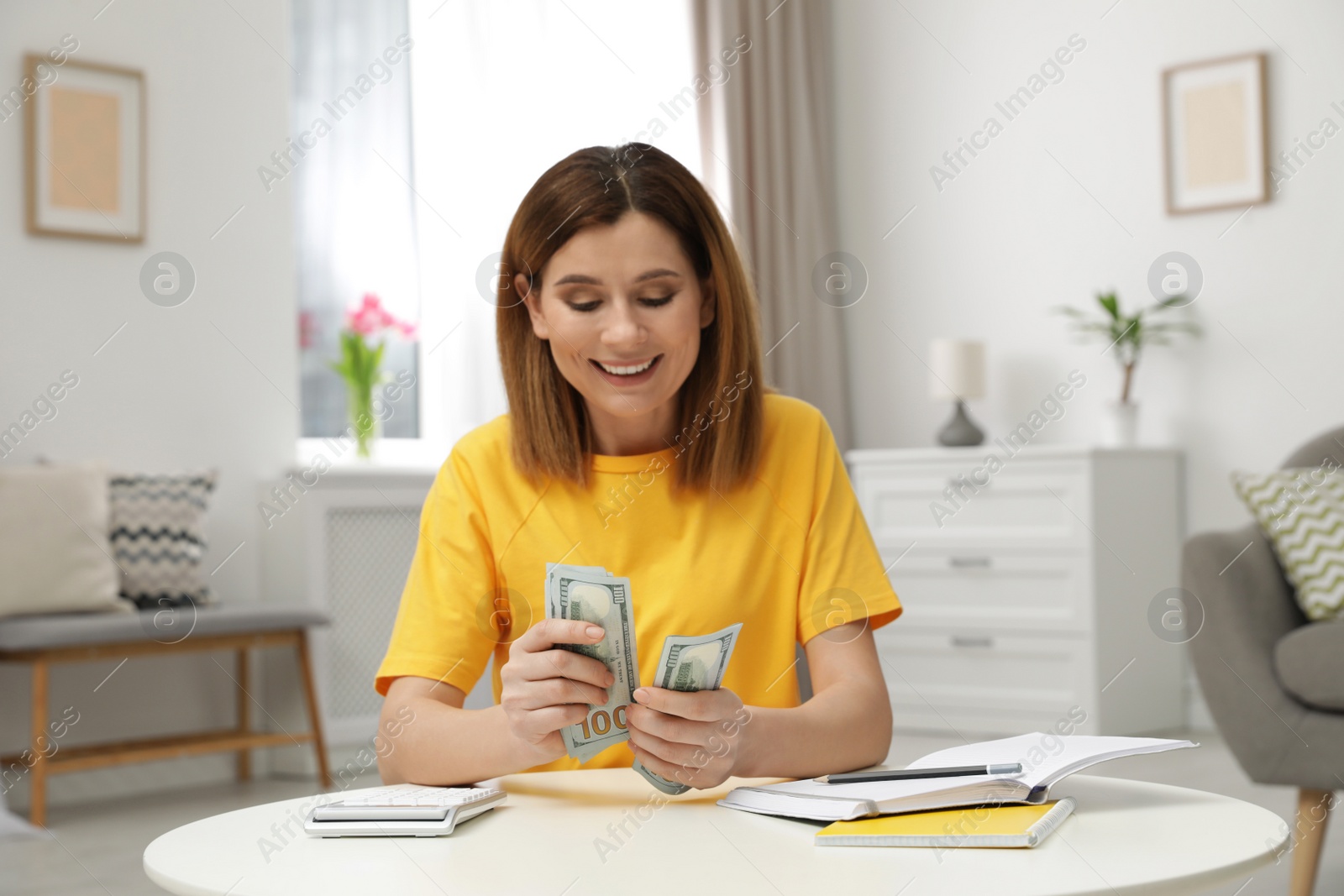 Photo of Smiling woman counting money at table indoors