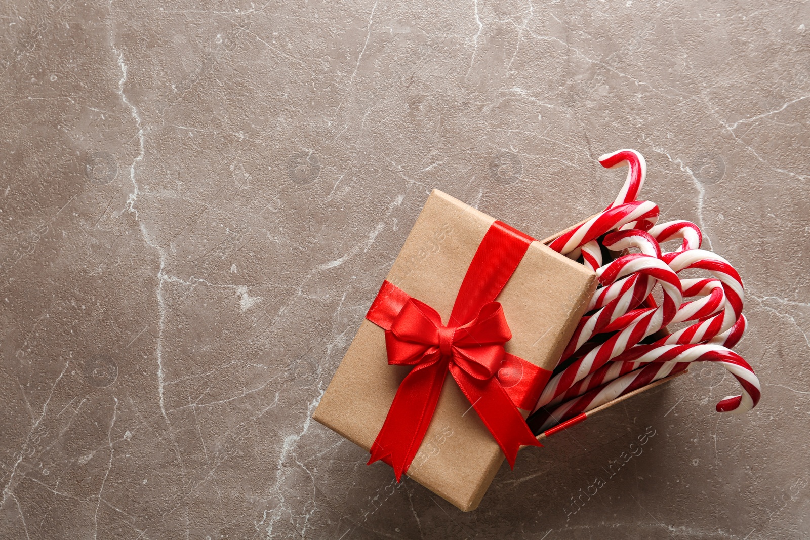 Photo of Candy canes in gift box on grey marble background, top view with space for text. Traditional Christmas treat