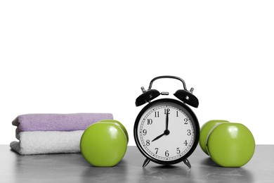 Photo of Alarm clock, towels and dumbbells on marble table against grey background. Morning exercise