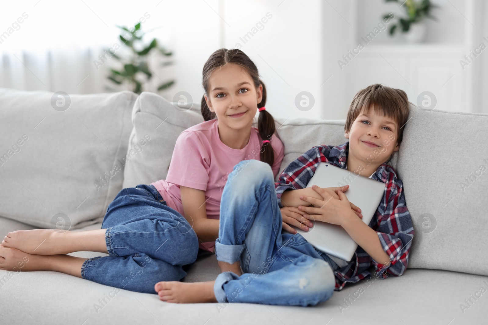 Photo of Happy brother and sister with tablet on sofa at home