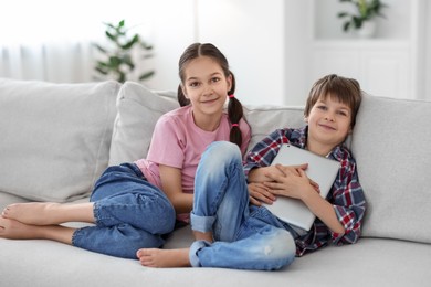 Happy brother and sister with tablet on sofa at home