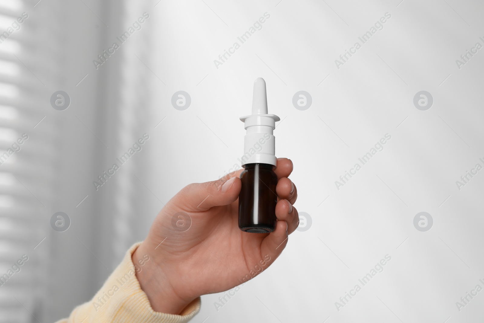 Photo of Woman holding nasal spray indoors, closeup view