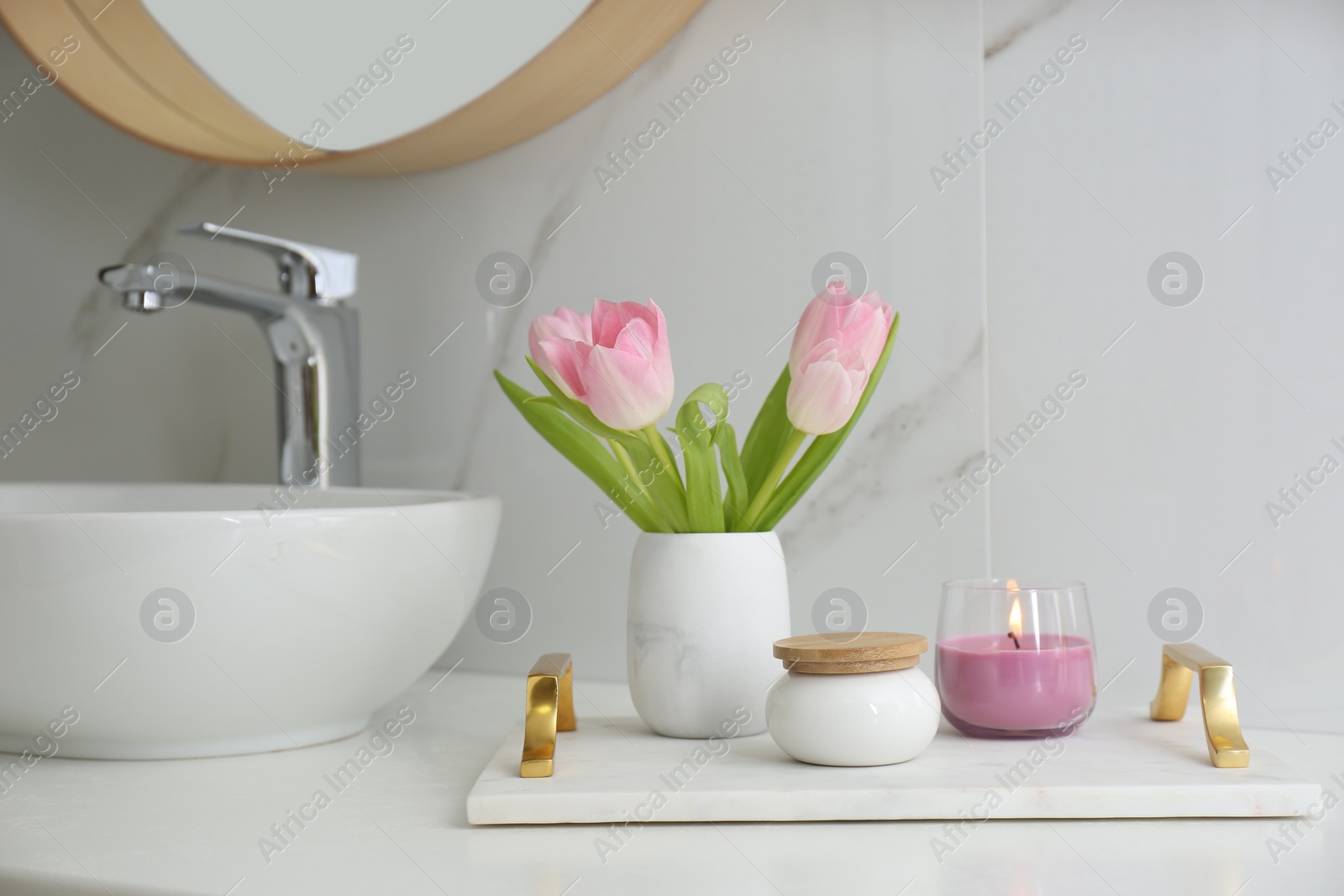 Photo of Beautiful flowers and candle on countertop in bathroom. Interior decor