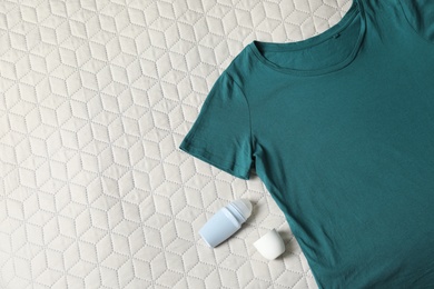 Roll-on deodorant and dark green t-shirt on light plaid, flat lay. Space for text