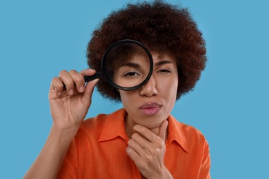 Photo of Young woman looking through magnifier glass on light blue background