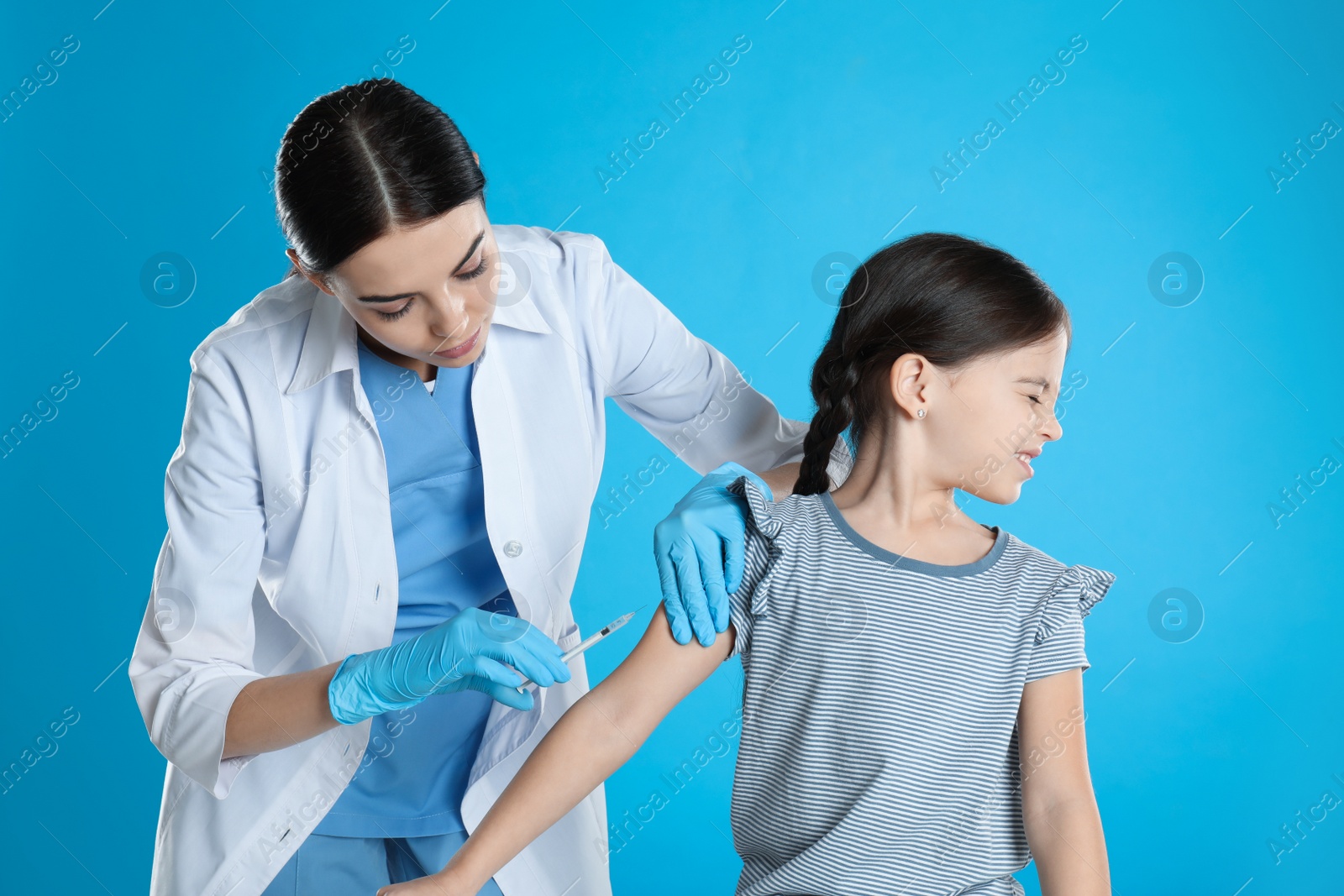 Photo of Doctor vaccinating little child on light blue background