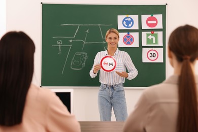 Teacher showing No Overtaking road sign near chalkboard during lesson in driving school