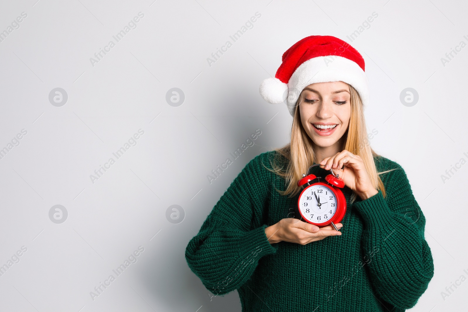 Photo of Woman in Santa hat with alarm clock on white background, space for text. New Year countdown