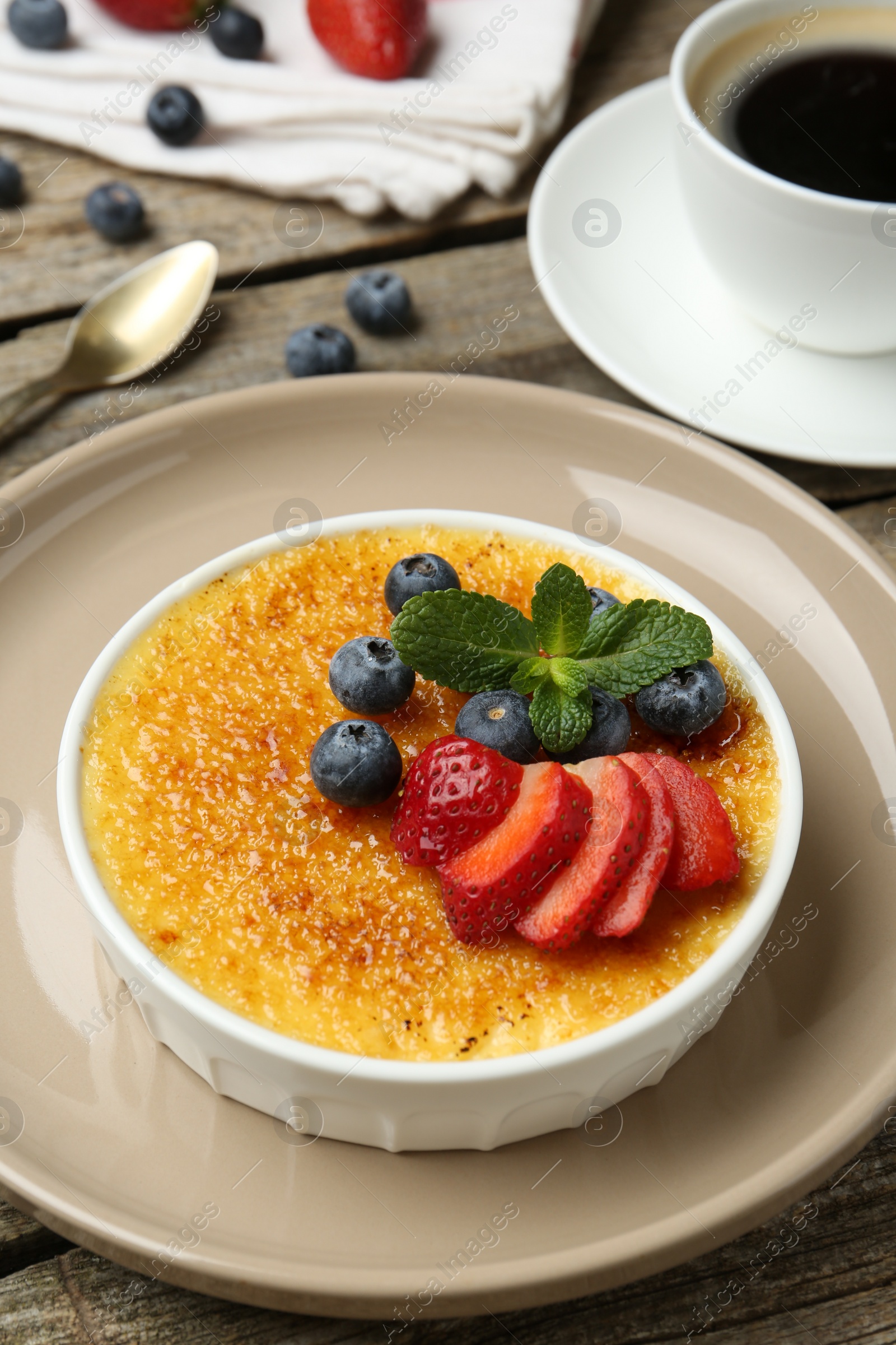 Photo of Delicious creme brulee with berries and mint in bowl on wooden table, closeup