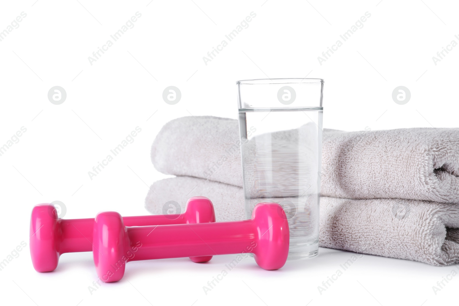 Photo of Stylish dumbbells, glass of water and towels on white background. Home fitness