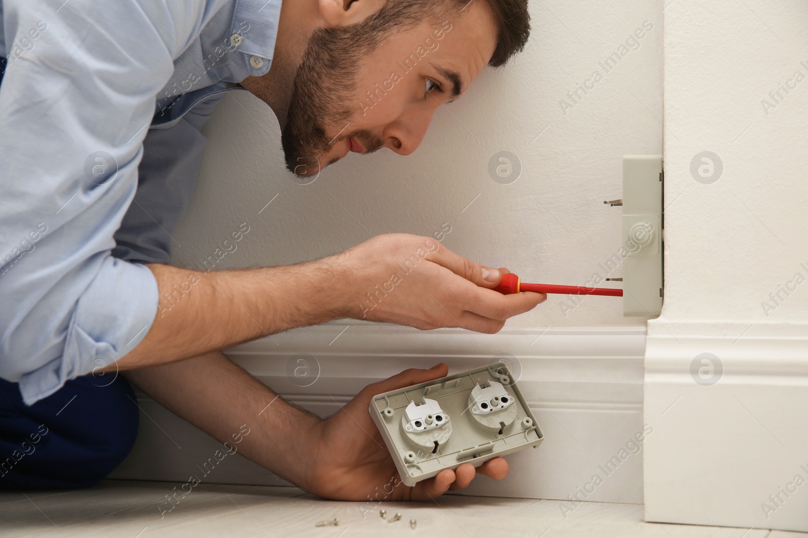 Photo of Electrician with screwdriver repairing power socket indoors, closeup