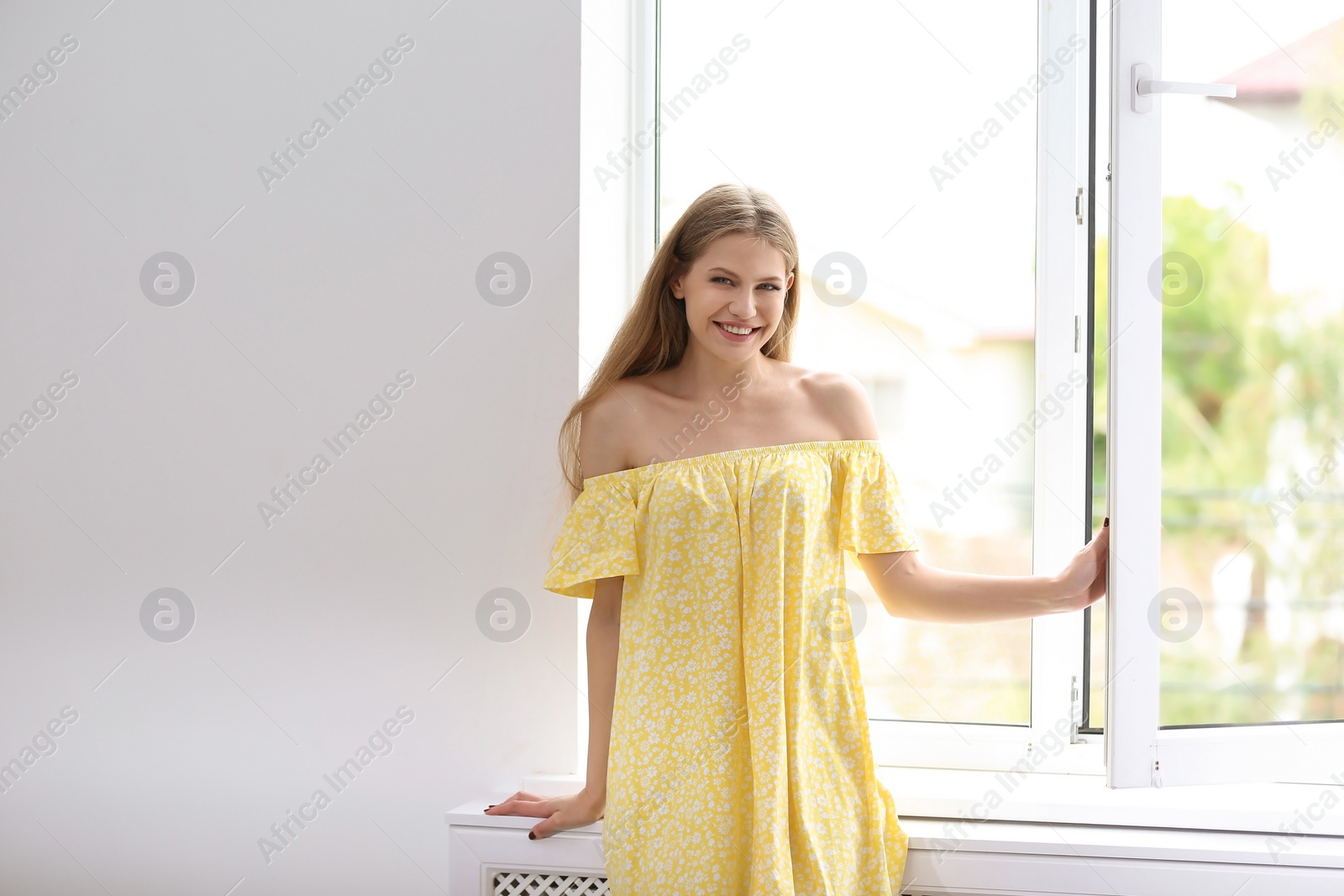 Photo of Young beautiful woman opening big window in room