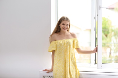 Young beautiful woman opening big window in room