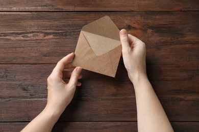 Photo of Woman with kraft paper envelope at wooden table, top view