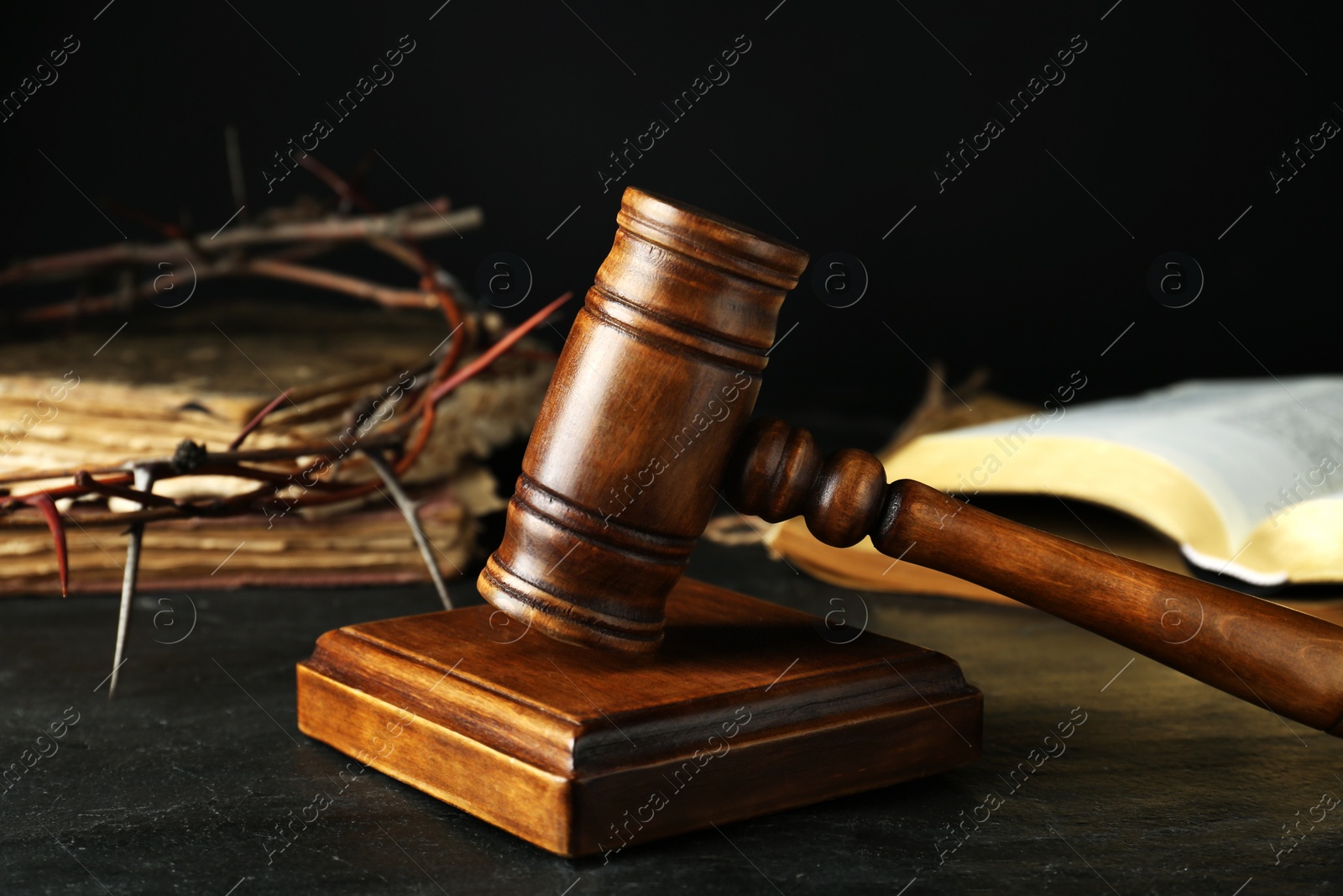 Photo of Wooden judge gavel and crown of thorns on black table, closeup