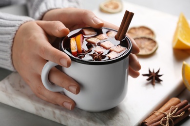 Photo of Woman holding mug with hot mulled wine on table, closeup