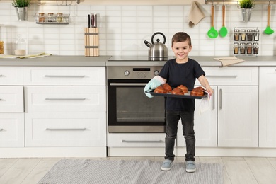 Photo of Little boy with tray of oven baked buns in kitchen