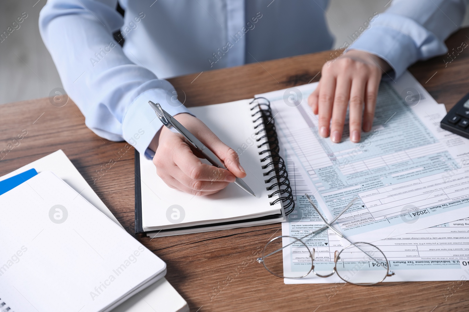 Photo of Payroll. Woman taking notes in notebook while working with tax return forms at wooden table, closeup