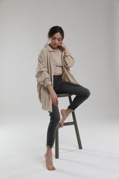 Portrait of beautiful woman sitting on chair against light grey background