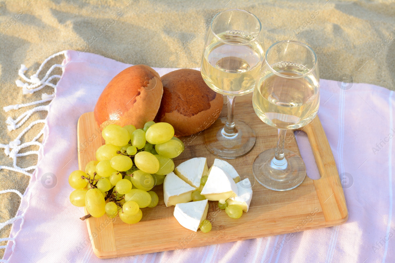 Photo of Glasses with white wine and snacks for beach picnic on sand outdoors