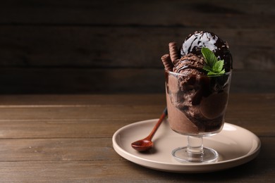 Delicious chocolate ice cream with wafer sticks, donut and mint in glass dessert bowl on wooden table. Space for text