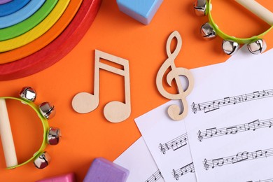 Photo of Tools for creating baby songs. Flat lay composition with wooden notes and tambourines for kids on orange background