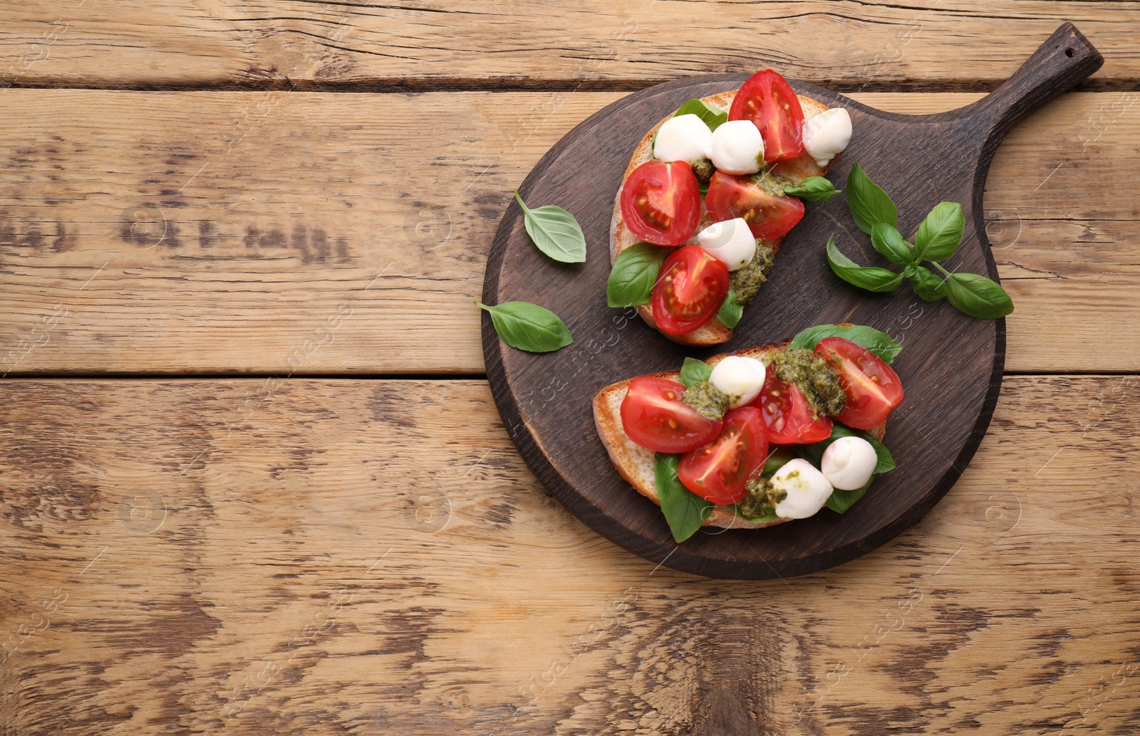 Photo of Delicious Caprese sandwiches with mozzarella, tomatoes, basil and pesto sauce on wooden table, top view. Space for text