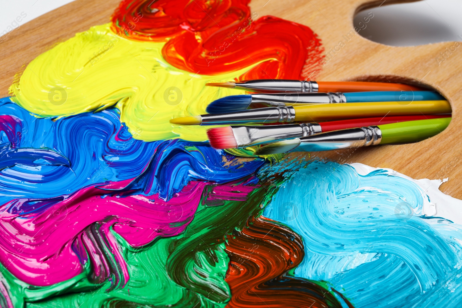 Photo of Palette with colorful acrylic paint and brushes on white background, closeup view