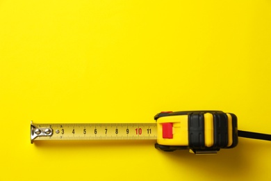 Photo of Tape measure on yellow background, top view. Space for text