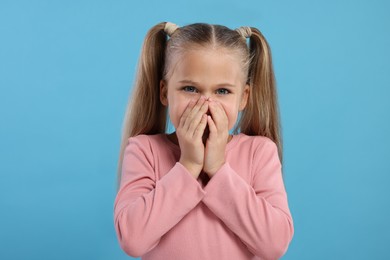 Photo of Embarrassed little girl covering her mouth with hands on light blue background