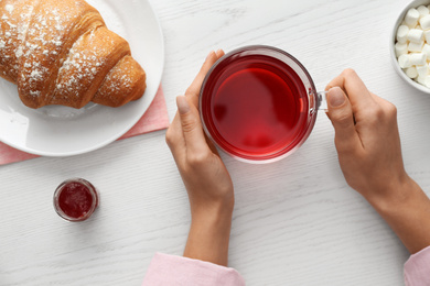 Photo of Woman holding glass cup of raspberry tea at white wooden table, top view. Delicious morning meal