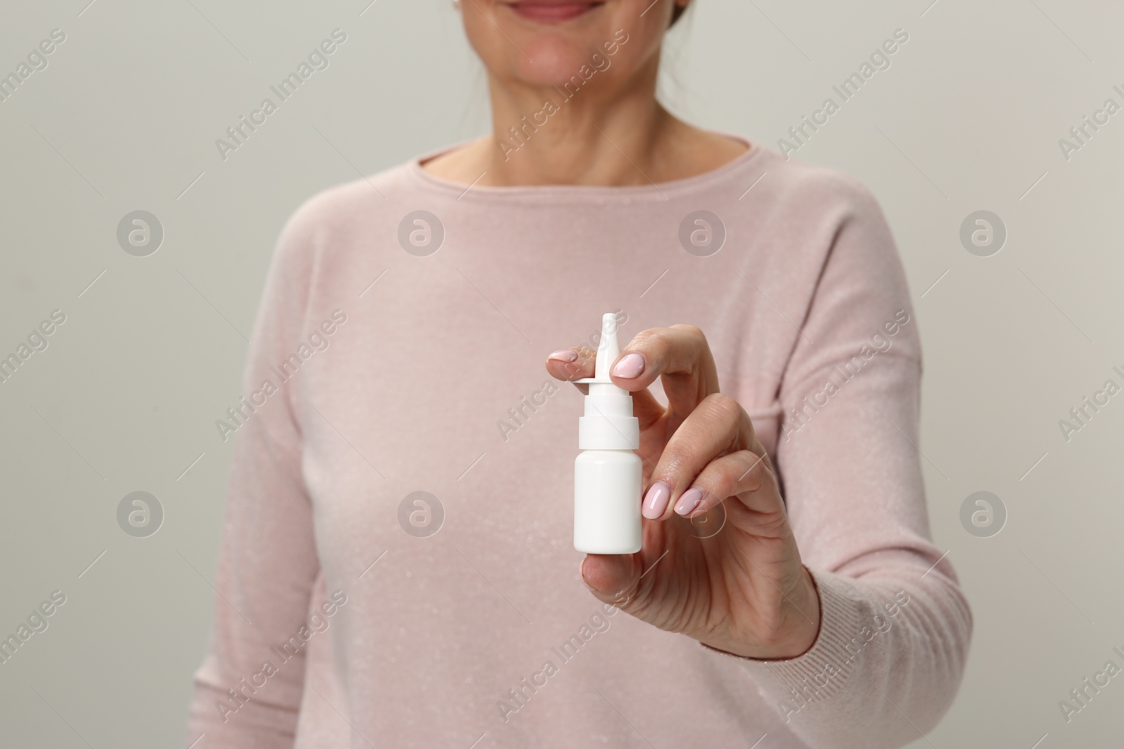 Photo of Woman holding nasal spray against light grey background, closeup