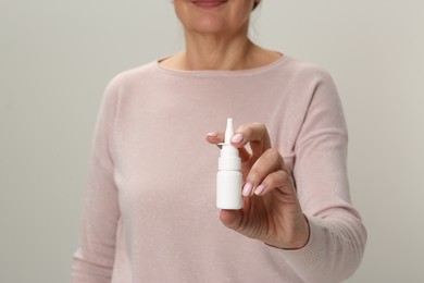 Woman holding nasal spray against light grey background, closeup