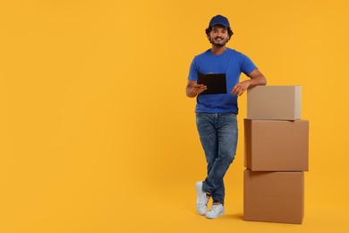 Happy courier with clipboard and stack of parcels on orange background, space for text