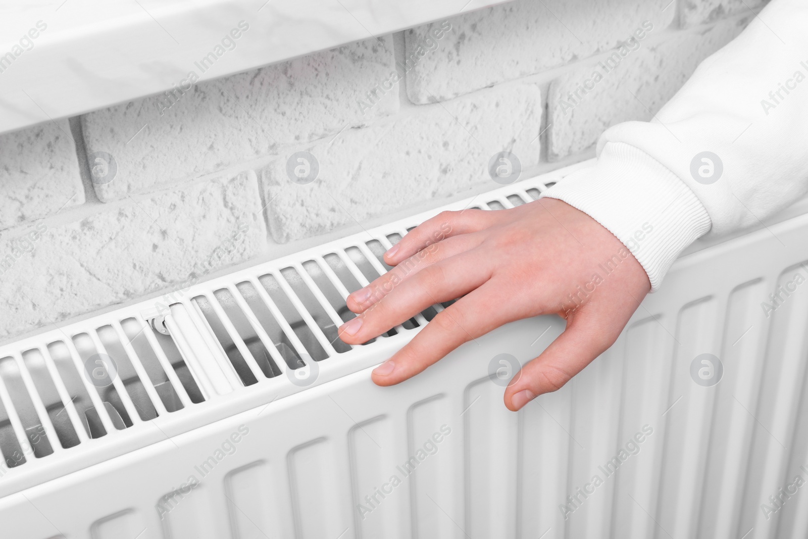 Photo of Girl warming hand on heating radiator indoors, closeup