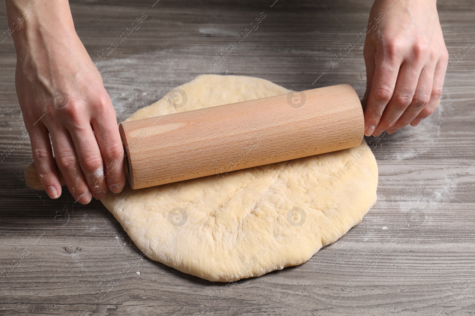 Photo of Woman rolling raw dough at wooden table, closeup