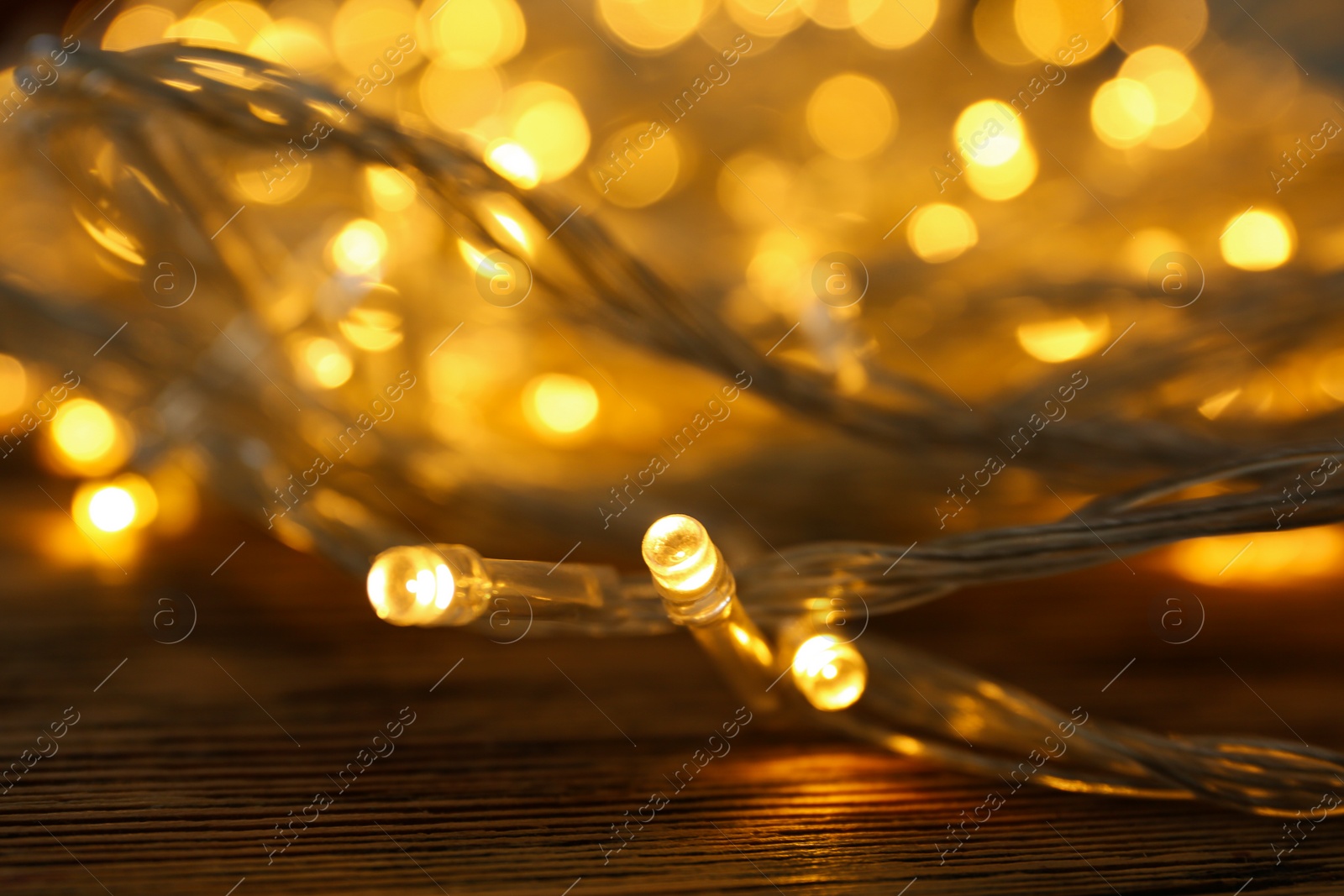 Photo of Glowing Christmas lights on wooden table, closeup view