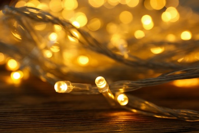 Glowing Christmas lights on wooden table, closeup view