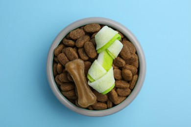 Photo of Dry dog food and treats (chew bones) on light blue background, top view