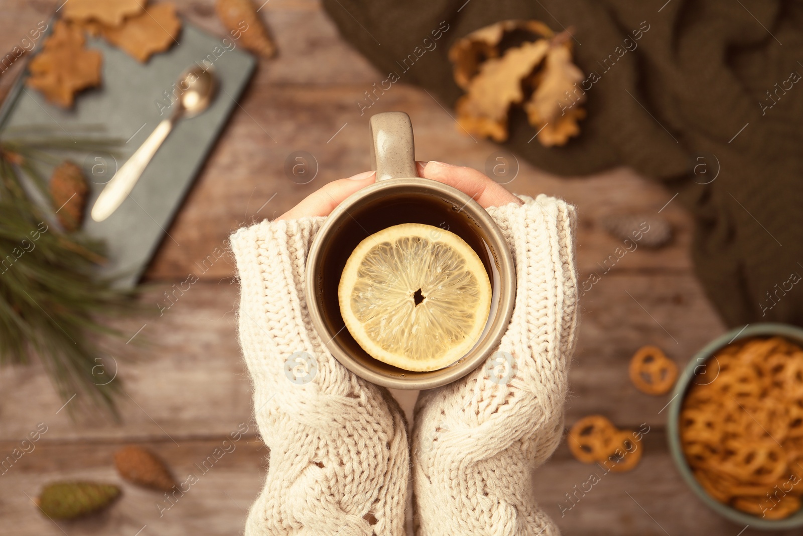 Photo of Woman in autumn sweater holding cup of hot cozy drink over wooden table, top view