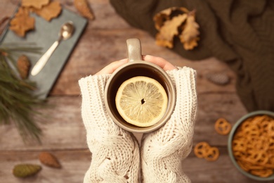 Photo of Woman in autumn sweater holding cup of hot cozy drink over wooden table, top view