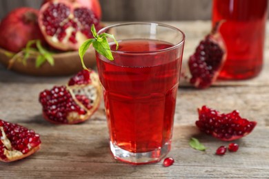 Photo of Tasty pomegranate juice in glass and fresh fruits on wooden table, closeup