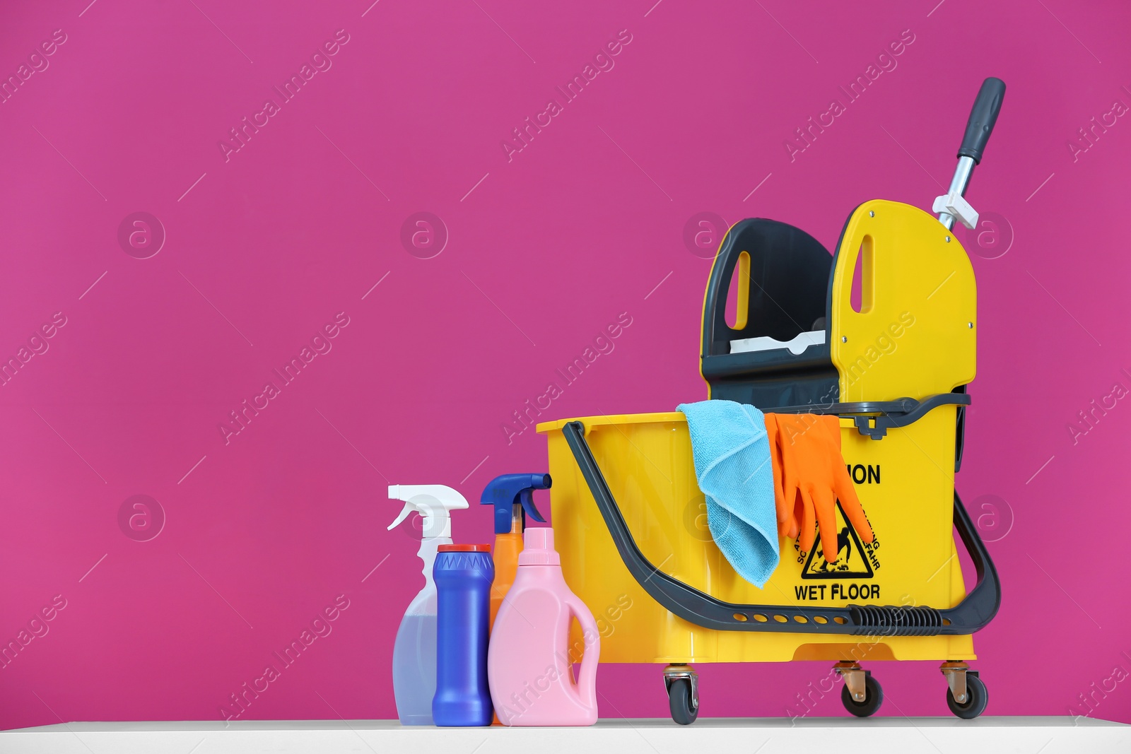 Photo of Mop bucket with cleaning supplies on color background