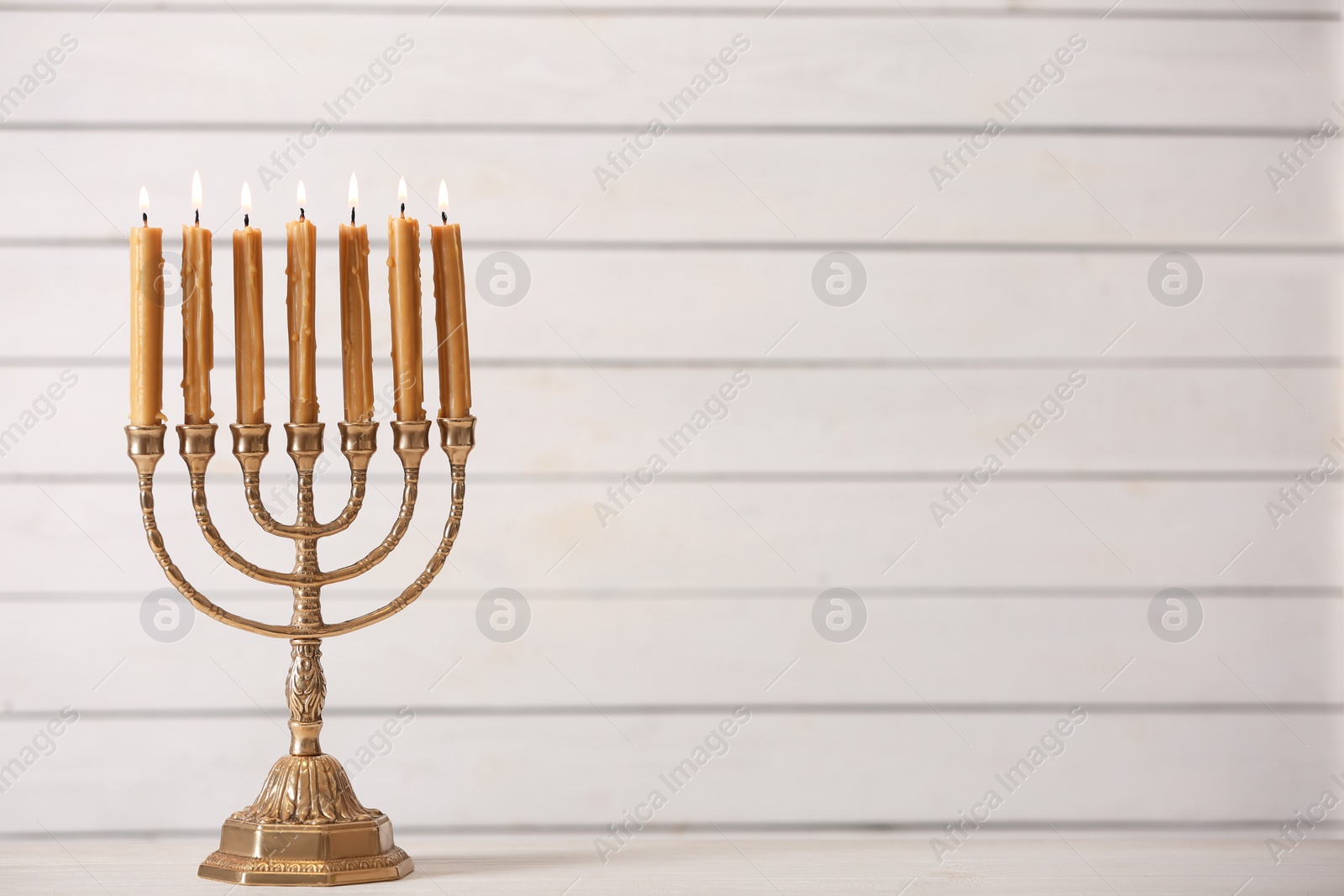 Photo of Golden menorah with burning candles on table against light background, space for text