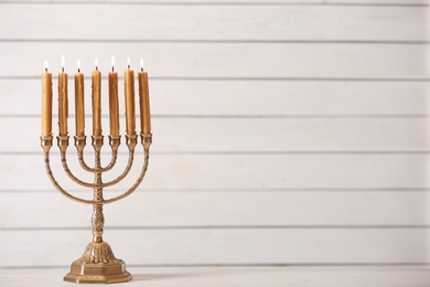 Photo of Golden menorah with burning candles on table against light background, space for text
