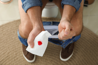 Photo of Man holding toilet paper with blood stain in rest room, closeup. Hemorrhoid concept